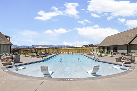 an outdoor pool with chairs and tables and a building with mountains in the background